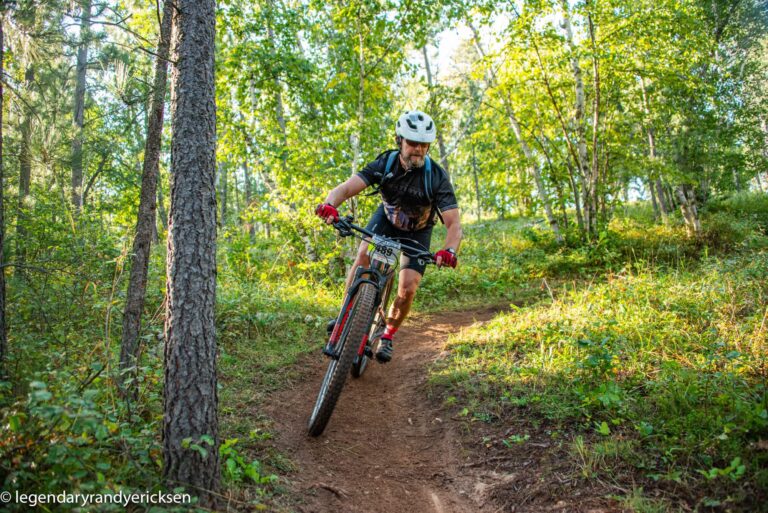 An action shot of a man in full gear mountain biking down a trail through the woods in South Dakota